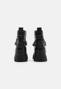 Botas de tobillo de cuero negro con suelas gruesas, con detalles de cadenas y una marca en relieve en los tacones. Acabado texturizado y diseño robusto.