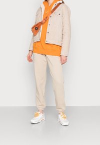 Beige corduroy jacket, orange hoodie, beige sweatpants, white sneakers with orange accents, and a brown crossbody bag.
