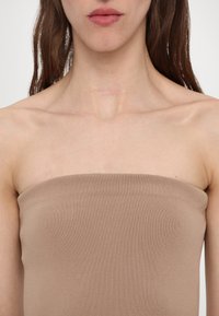 Suknelė be petnešų šviesiai beigėje spalvoje, pagaminta iš raštuoto audinio. Turinti prigludusį dizainą su lygia tekstūra ir be matomų detalių.