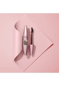 Mascara Maybelline Lash Sensational in un tubetto metallico rosa accanto a un pennello abbinato, su uno sfondo rosa con texture liscia.