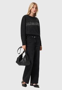 Czarny sweter z napisem z rhinestone'ów, czarne jeansy z wysokim stanem, płaskie czarne buty oraz czarna torebka. Gładki materiał, luźny krój.