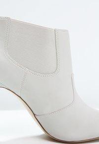 Witte enkelboot met een bovenwerk van glad leer en een elastische zijpaneel. Beschikt over een ronde neus en een slank ontwerp met minimale stiksels.