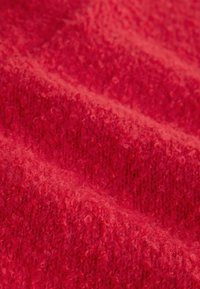 Gros plan sur un tissu tricoté texturé de couleur rouge vif avec des fibres douces et duveteuses et un motif côtelé visible créant des lignes diagonales.