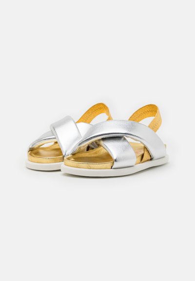 Sandali metallici argento con cinturini incrociati, dettagli gialli e suola piatta bianca. Design open-toe, con interno dorato.