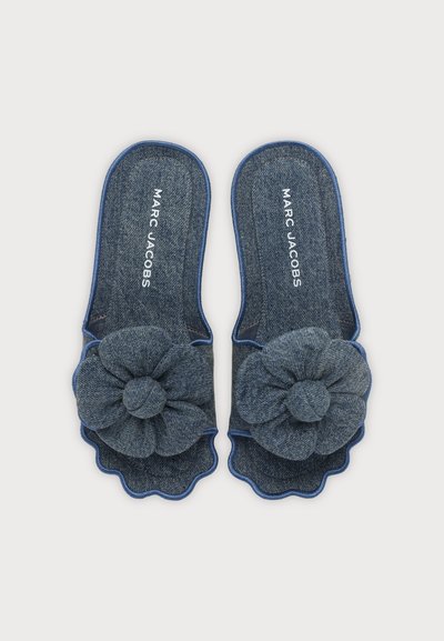 Chaussons bleu denim à bout ouvert avec grandes décorations florales en tissu et bords festonnés, estampillés "MARC JACOBS" sur les semelles intérieures.