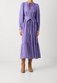 Lilla blomstrede maxikjole med lange ærmer, rynket krop og taljebånd. Har flæsekant forneden, kombineret med lysebrune ankelstøvler.