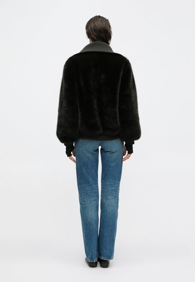 Giacca in pelliccia sintetica nera con ampio colletto, abbinata a jeans in denim azzurro chiaro. La giacca ha una vestibilità comoda e polsini a coste.