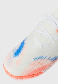 Weißer Sportschuh mit einem strukturierten Obermaterial in einem blauen und korallenfarbenen Muster, weißen Schnürsenkeln und einer lebhaften orangenen Sohle.