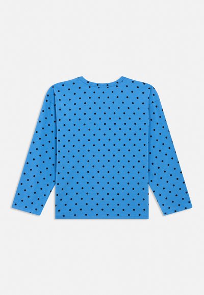 Blå langermet skjorte med rund hals, dekket med jevnt fordelte små svarte polkadotter, lagt flatt på en hvit bakgrunn.