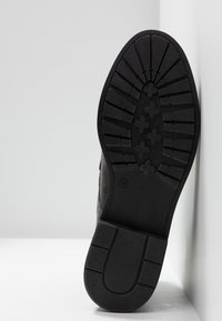 Semelle de chaussure en caoutchouc noir avec un motif de bande de roulement texturé. Bout arrondi et talon surélevé, taille 38 marquée, avec un bord lisse et un design plat.