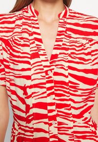 Femme portant une robe boutonnée à manches courtes et col avec un motif zèbre rouge et blanc cassé.