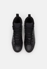 Een paar zwarte hoge sneakers met veters, rubberen neusbeschermers en stoffen trekkoorden op een witte achtergrond, van bovenaf bekeken.