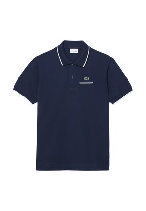 Mørkeblå bomulds polo med hvid kant på kraven og ærmerne. Har et lille grønt krokodillelogo og en lomme på brystet.