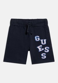 Σκούρο μπλε σορτς με ελαστική ζώνη μέσης και κορδόνι, με πλευρικές τσέπες και γράμματα "GUESS" σε μπλε και άσπρο σε ένα πόδι.