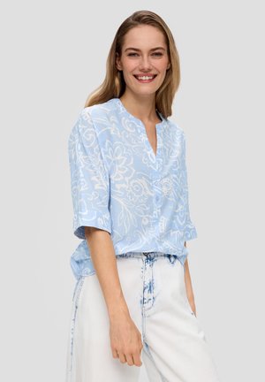 Lichtblauwe bloempatronenblouse met een Mandarin-kraag, korte mouwen en knoopdetails, gecombineerd met witte spijkerbroek.