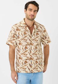 Camicia a maniche corte realizzata in tessuto leggero, con una base beige decorata da motivi floreali marroni e blu, e un colletto stile camp.