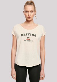 Modell trägt ein hellcremefarbenes T-Shirt mit dem Aufdruck "DRIVING GO NORTH" und einer Illustration eines Autos, das einen Baum transportiert, kombiniert mit schwarzen Leggings.