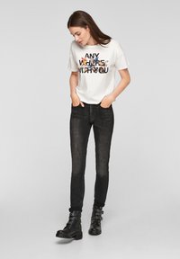 T-shirt blanc avec un graphique de papillon coloré et une inscription noire, associé à un jean skinny noir et des bottes de combat noires avec des accents cloutés.