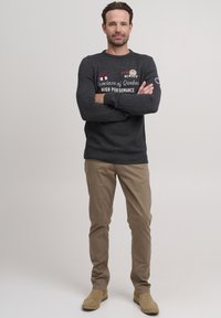 Mörkgrå stickad tröja med text och lappar, i kombination med beige byxor och bruna ankelstövlar. Tröjan har ribbade muddar och nederdel.