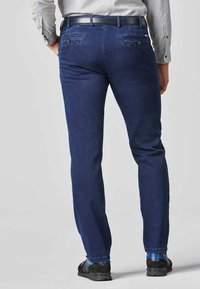 Dunkelblaue Denim-Jeans im Slim-Fit-Stil, mit zwei Gesäßtaschen und einer glatten Textur, kombiniert mit einem schwarzen Gürtel und schwarzen Schuhen.