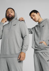 Graue Kapuzenshirts mit Fronttaschen, versehen mit schwarzen Puma-Logos. Der Stoff wirkt weich, hat eine lässige Passform und gerippte Ärmelbündchen.