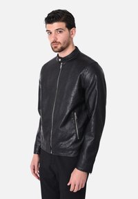 Giacca in pelle nera con colletto alto, chiusura frontale con zip e tasche laterali con zip. Texture liscia con un design aderente.