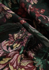 Donkere stof met geplooide elastische details, versierd met een bloemenpatroon in tinten van rood, roze, groen en beige.