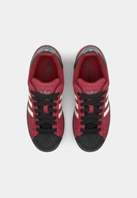 Red suede sneakers with black rubber toe cap and laces. Features three white lateral stripes and embossed logo on the tongue.