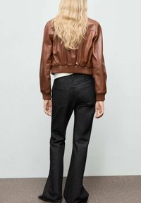 Chaqueta bomber de cuero marrón con puños y dobladillo acanalados, combinada con pantalones de mezclilla oscuros de tiro alto y campana. El modelo se ve desde atrás.