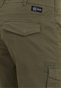 Pantalons cargo vert olive en tissu texturé, avec une poche arrière et une étiquette de marque noire. Les détails de couture sont visibles.