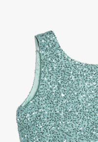 Haut sans manches bleu clair densément recouvert de petites paillettes brillantes sur un fond blanc uni.