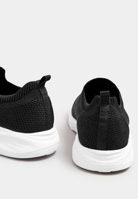 Schwarze Netz-Sportschuhe mit strukturiertem Obermaterial, elastischem Kragen und einer kontrastierenden weißen Gummisohle. Mit einer Ziehschlaufe an der Rückseite.