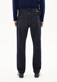 Jeans de mezclilla azul oscuro con corte recto, que presentan una etiqueta en la cinturilla y dos bolsillos traseros, mostrados desde la parte trasera.