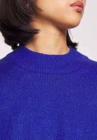 Närbild av en person som bär en ljusblå stickad tröja med rakt mörkt hår, som visar hals och nedre del av ansiktet.