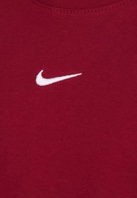 Bordo medvilnės marškinėliai su apvaliu kaklu ir maža balta Nike swoosh logotipu išsiuvinėtu priekyje. Sklandus, kvėpuojantis paviršius.