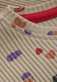 Geribbelde beige stof met een rode kraag heeft kleurrijke patronen van harten en muffins in oranje, paars en rood.