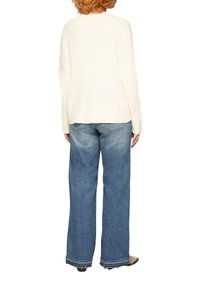 Cremfarbener, gerippter Strickpullover mit überschnittenen Schultern, getragen zu weit geschnittenen blauen Jeans mit fransigem Saum und subtiler Ausbleichung.