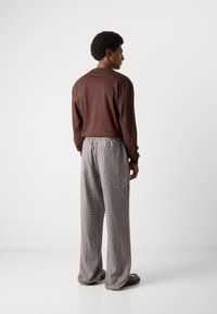 Chemise marron à manches longues avec une coupe décontractée, associée à un pantalon large à motifs noir et blanc ; tissu doux et taille élastique.