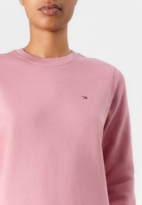 Pink sweatshirt made of soft fabric, featuring a crew neckline and ribbed cuffs. A small logo is positioned on the left chest area.