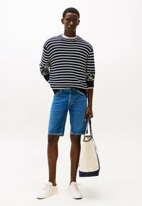 Marineblauw en witte gestreepte trui, blauwe denim shorts, witte sneakers en een lichtgekleurde totebag met marineblauwe accenten.