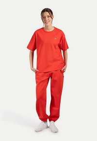 Röd bomulls-t-shirt med korta ärmar och rund halsringning, kombinerad med matchande röda sweatpants med elastiska muddar och diskreta logodetaljer.