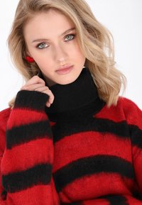 Pulover cu guler înalt, dungi roșii și negre, dintr-un tricot moale și texturat. Are un guler înalt și mâneci late.