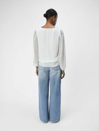 Blouse blanche plissée à manches longues avec un col rond, associée à un jean large taille haute bleu clair, vue de dos.
