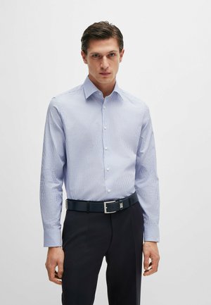 Camicia a righe blu chiaro e bianca con maniche lunghe, colletto button-down, abbinata a una cintura scura, indossata con pantaloni scuri.