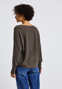Maglione a maglia marrone con una vestibilità rilassata, spalle scese e polsini a coste, abbinato a jeans in denim blu, visto da dietro.