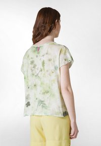 Top de manga corta en tejido ligero con estampado floral en verde y beige. Cuello redondo con una pequeña etiqueta rosa en la parte de atrás.