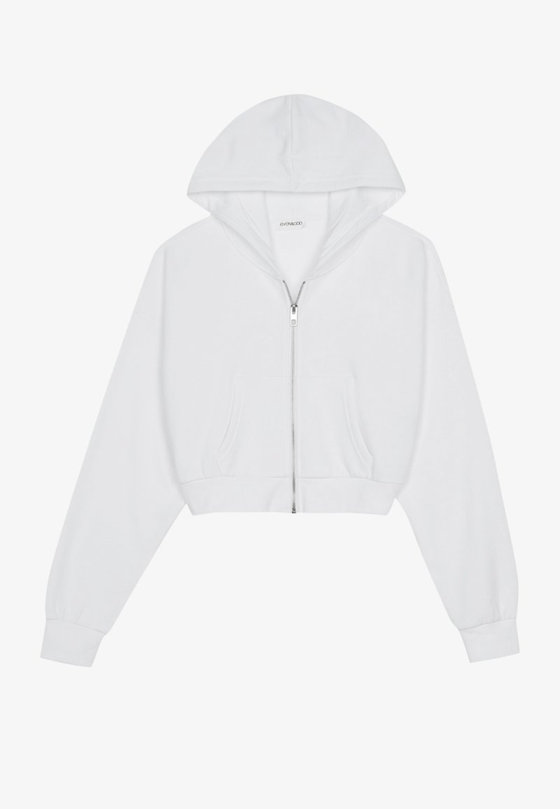 Haut de survêtement cropped blanc avec une fermeture éclair à l'avant, des manches longues, des poches latérales et une capuche. Fabriqué en tissu doux avec une texture lisse.