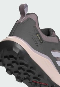 Zapato de senderismo gris con acentos rosas, parte superior de malla, suela de goma texturizada y agarre Traxion, con una etiqueta Gore-Tex en el lateral.