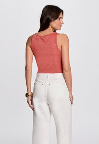 Red fitted tank top with a subtle shimmer, paired with high-waisted white wide-leg jeans. Smooth texture and minimal hardware details.