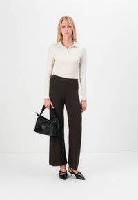 Women’s ribbed long-sleeve top in cream, paired with brown textured wide-leg pants. Black handbag, pointed-toe black heels with bow detail.